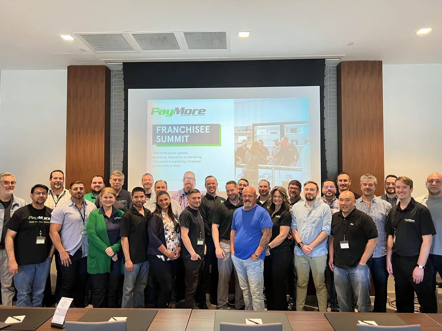 Empowering-Franchisees-PayMore-Electronics-Launches-Successful-First-Annual-Franchisee-Summit A large group of people standing with a large screen behind them
