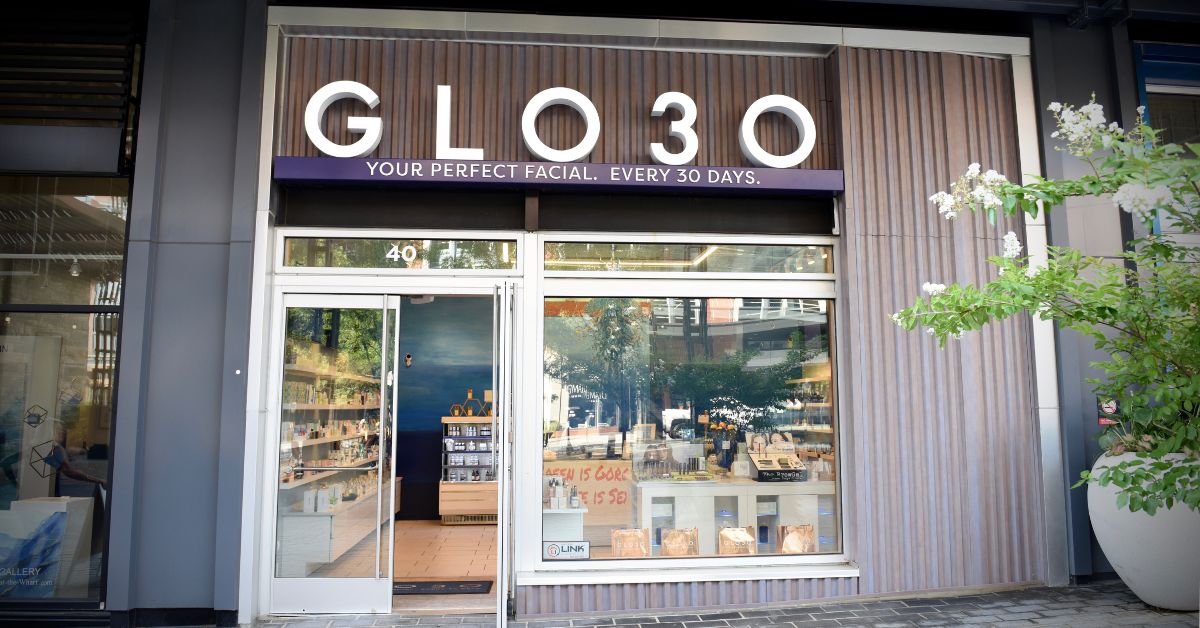 glo30-membership-based-skincare-studio-headlines-may-2024 A storefront with dark wood slats on its exterior. In white lettering, the sign reads 'GLO30. Your perfect facial. Every 30 days.' The entrance consists of glass doors with window panels. glo30 membership based skincare studio headlines may 2024