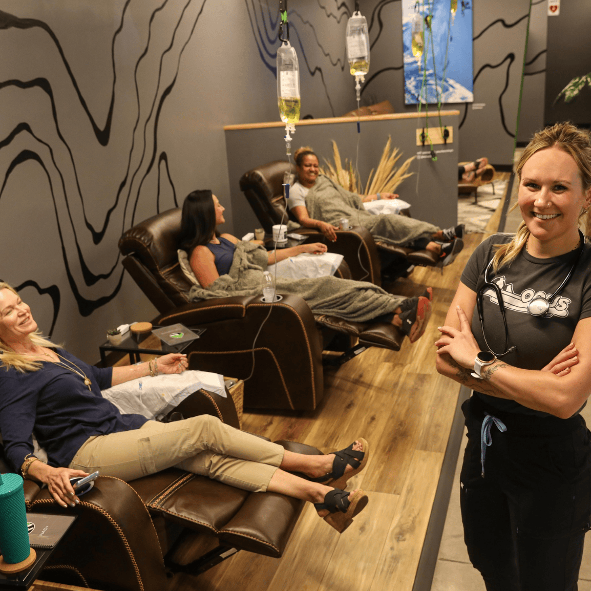 The Onus IV therapy franchise lounge with ER nurse with folded arms and stethoscope around her neck standing front of people getting treatments in lounge chairs