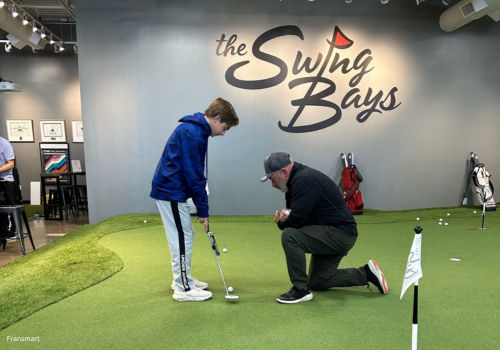 A golf instructor giving a kid a lesson at swing bays on the putting course