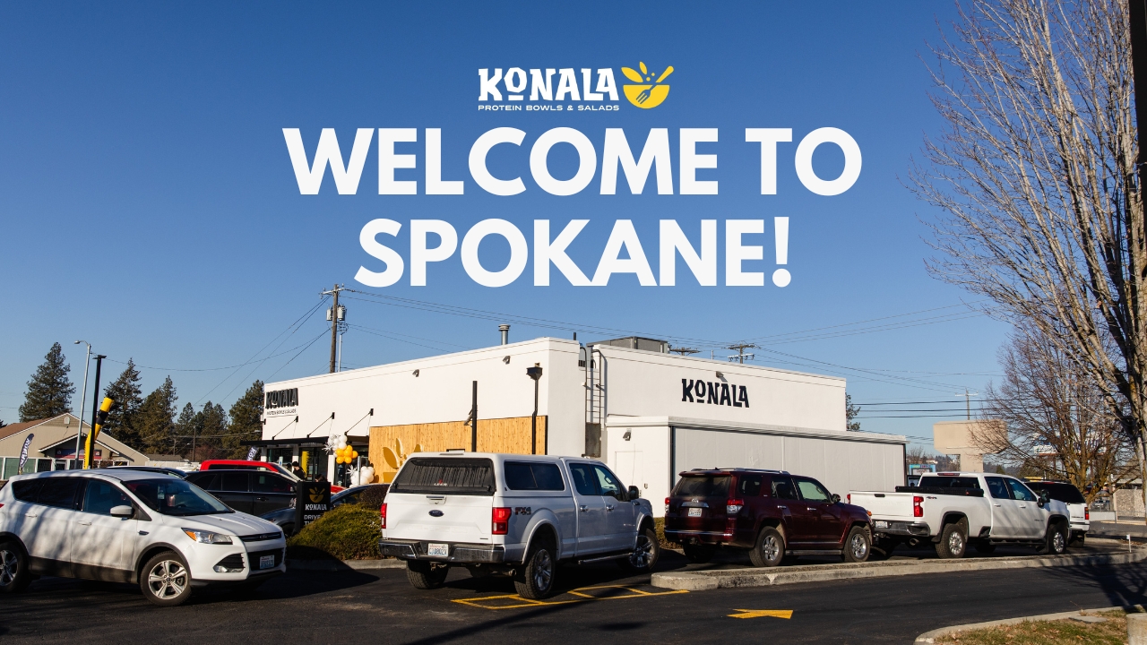 Exterior view of a Konala restaurant building with a parking lot in front, showcasing a bright blue sky. Large bold text overlays the image, reading 'WELCOME TO SPOKANE!' with the Konala logo above it.