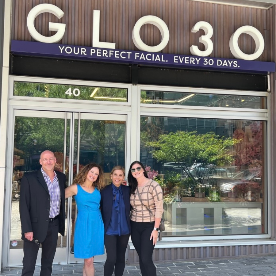 James and Andrea Robertson (left), GLO30 Founder, Dr. Arleen Lamba, and Abigail Freeland. Outdoors, standing together underneath a GLO30 skincare franchise sign.
